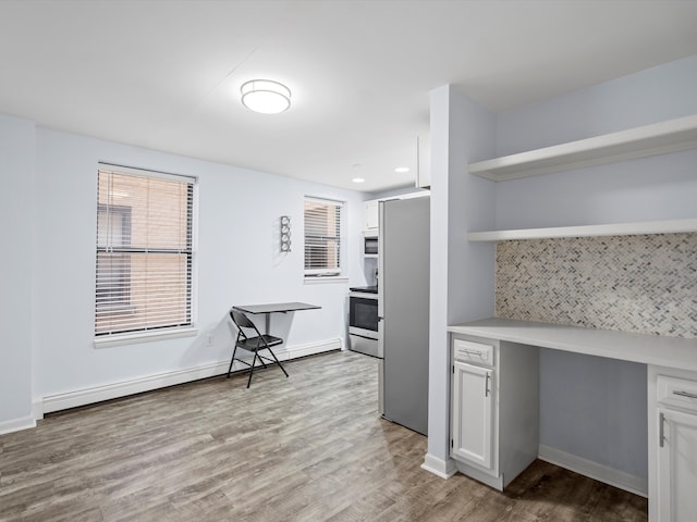 interior space with stainless steel fridge, built in microwave, built in desk, a baseboard radiator, and white cabinetry