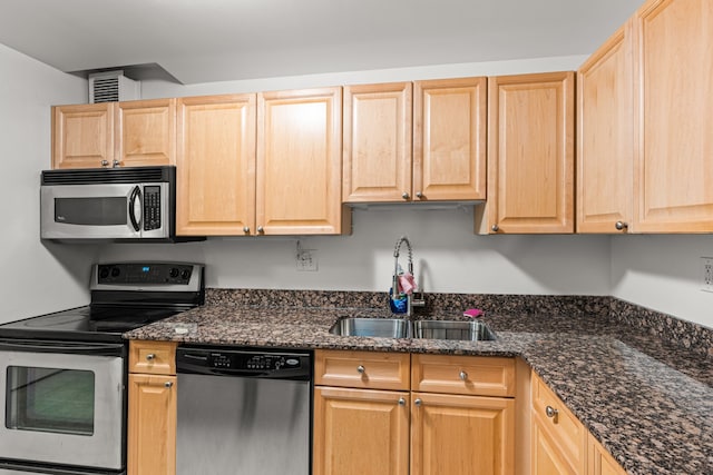 kitchen with appliances with stainless steel finishes, light brown cabinetry, dark stone countertops, and sink