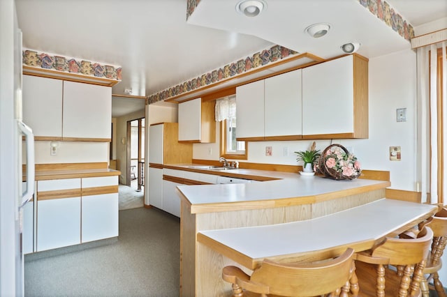 kitchen featuring light countertops, a peninsula, a breakfast bar area, and white cabinetry