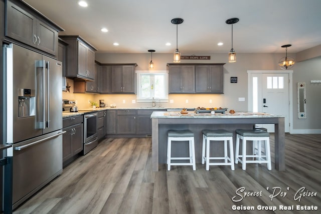 kitchen with hardwood / wood-style floors, a center island, light stone countertops, decorative light fixtures, and stainless steel appliances