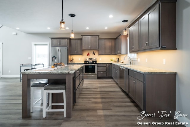 kitchen with a center island, light stone counters, dark hardwood / wood-style flooring, pendant lighting, and appliances with stainless steel finishes