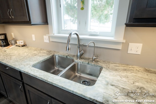 kitchen featuring light stone countertops, dark brown cabinetry, and sink