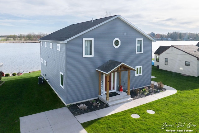 traditional-style home featuring a shingled roof, central AC unit, a water view, and a front lawn