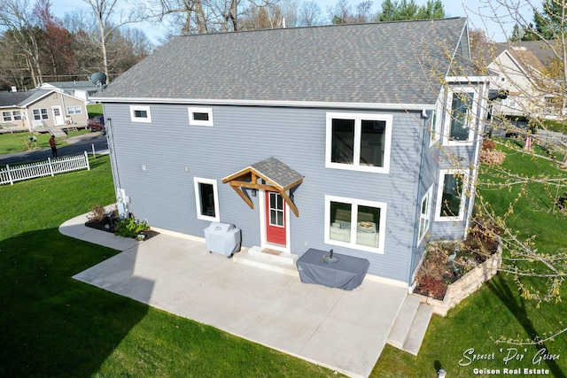 rear view of property featuring a patio, a shingled roof, a lawn, and fence