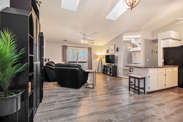 living room with ceiling fan, lofted ceiling with skylight, and wood-type flooring