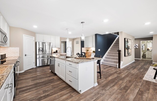 kitchen with a center island with sink, sink, pendant lighting, stainless steel appliances, and white cabinets