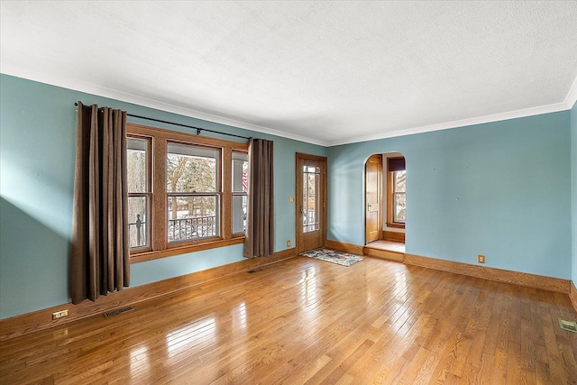 empty room with a textured ceiling, light wood-type flooring, and crown molding