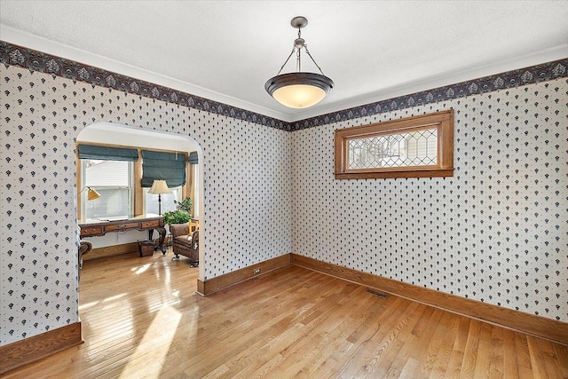 empty room featuring wood-type flooring, a textured ceiling, a wealth of natural light, and crown molding