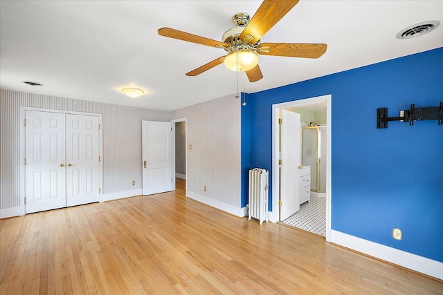 unfurnished bedroom featuring radiator, ceiling fan, ensuite bath, and light wood-type flooring