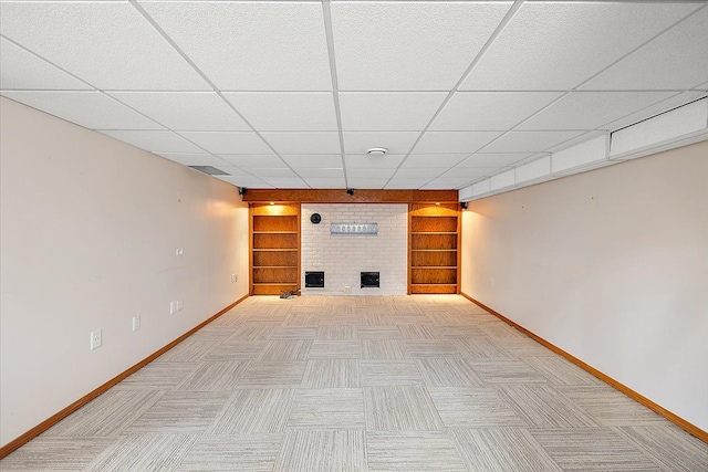 basement featuring built in shelves, a paneled ceiling, and a brick fireplace