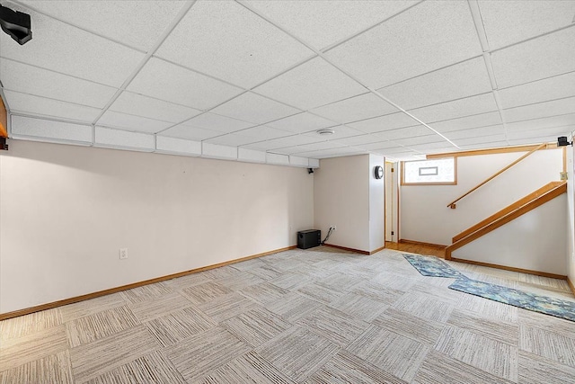 basement with a paneled ceiling and light colored carpet