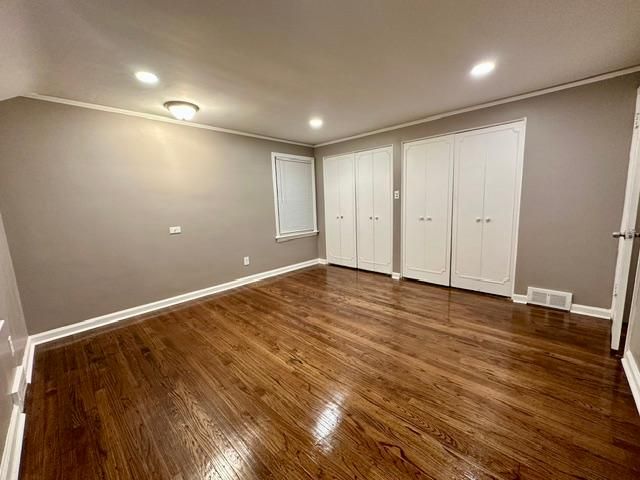 unfurnished bedroom with crown molding, dark wood finished floors, visible vents, and baseboards