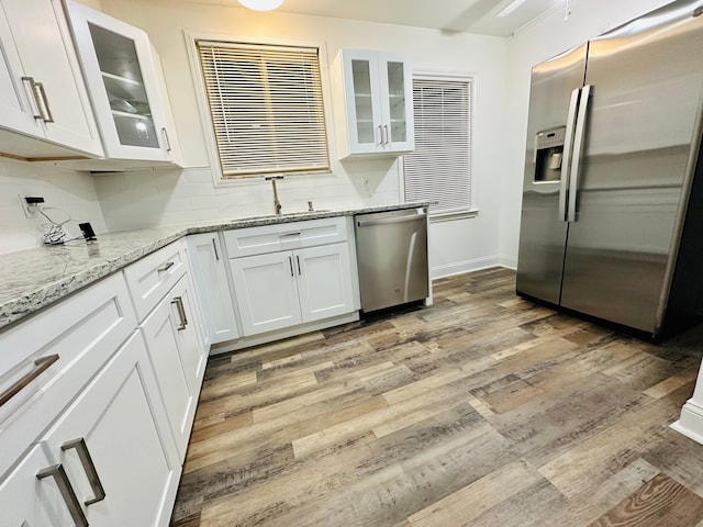 kitchen featuring sink, light hardwood / wood-style flooring, light stone countertops, appliances with stainless steel finishes, and white cabinets