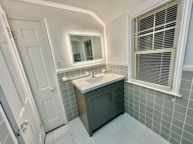 bathroom with lofted ceiling, vanity, tile walls, and tile patterned flooring