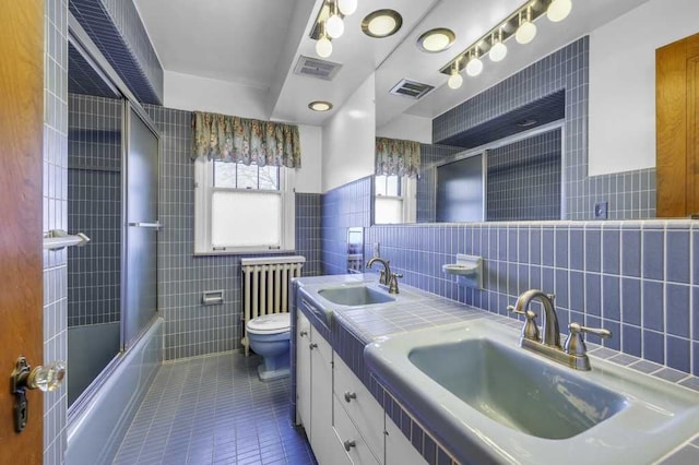 full bathroom featuring combined bath / shower with glass door, tile walls, tile patterned flooring, vanity, and toilet