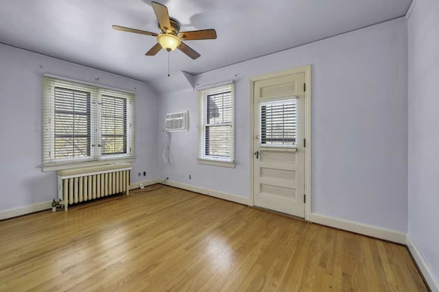 unfurnished room featuring a wall mounted air conditioner, radiator heating unit, light hardwood / wood-style floors, and ceiling fan