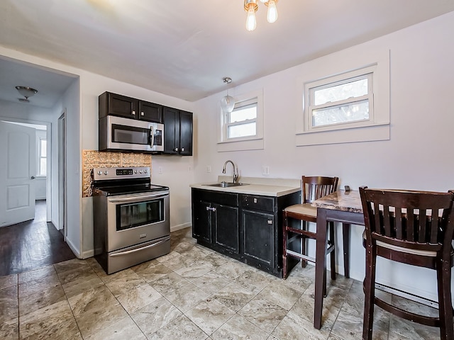 kitchen with backsplash, stainless steel appliances, hanging light fixtures, and sink