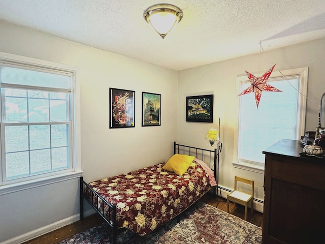 bedroom with dark hardwood / wood-style floors, a baseboard heating unit, a textured ceiling, and multiple windows