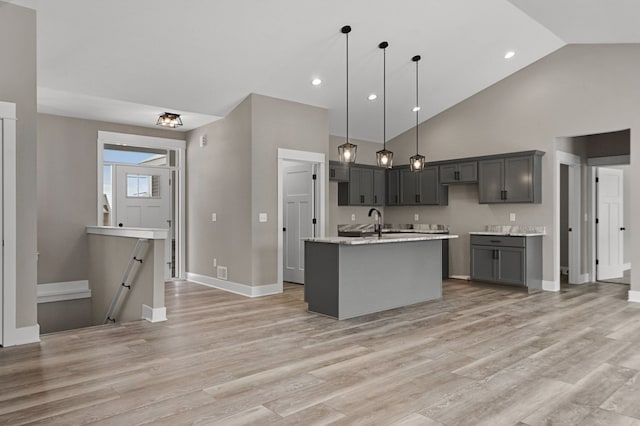 kitchen with gray cabinets, high vaulted ceiling, decorative light fixtures, light hardwood / wood-style floors, and a center island with sink