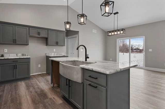 kitchen featuring sink, gray cabinetry, a center island with sink, pendant lighting, and hardwood / wood-style floors