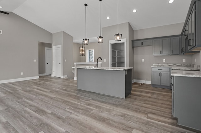 kitchen featuring gray cabinets, light stone countertops, an island with sink, and hanging light fixtures