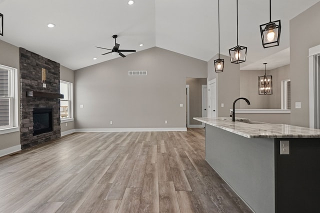 kitchen with a stone fireplace, sink, hanging light fixtures, light wood-type flooring, and ceiling fan