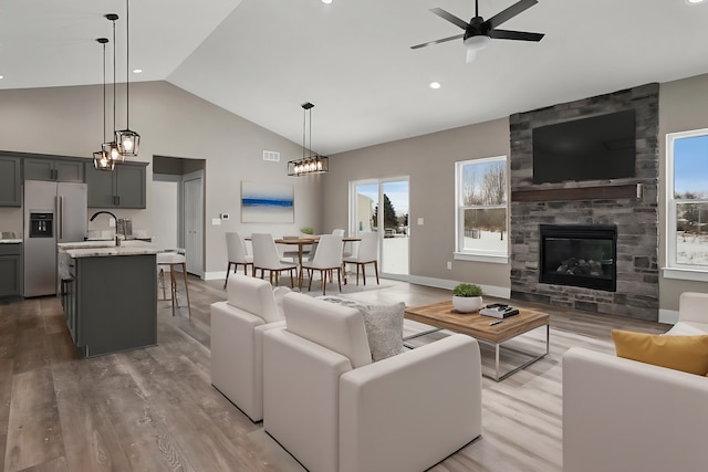 living room featuring high vaulted ceiling, wood-type flooring, a large fireplace, sink, and ceiling fan