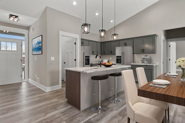 kitchen with gray cabinets, stainless steel refrigerator with ice dispenser, pendant lighting, and an island with sink