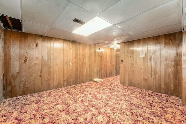 basement featuring carpet flooring, a paneled ceiling, and wood walls