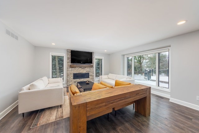 living room with a stone fireplace and dark wood-type flooring