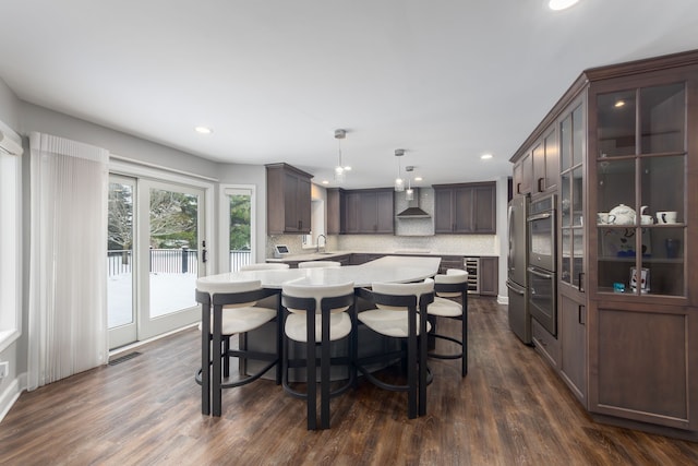 kitchen with pendant lighting, dark brown cabinetry, tasteful backsplash, and wall chimney range hood