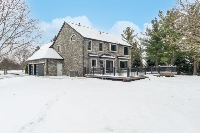 snow covered rear of property with a deck, a garage, and central air condition unit