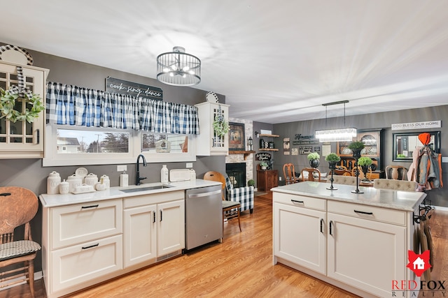 kitchen with dishwasher, sink, decorative light fixtures, a fireplace, and a notable chandelier