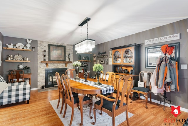 dining space with a fireplace, an inviting chandelier, and light wood-type flooring