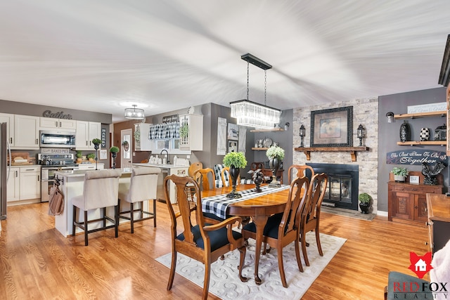 dining room featuring light wood-type flooring, a stone fireplace, a notable chandelier, and sink