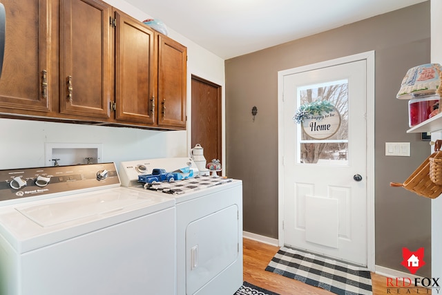 clothes washing area with washing machine and dryer, light hardwood / wood-style flooring, and cabinets