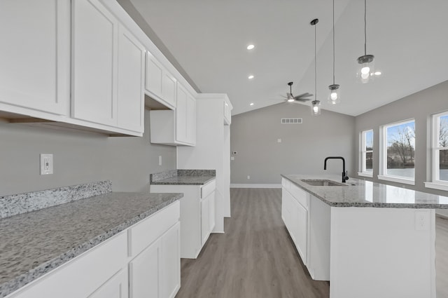 kitchen featuring stone counters, sink, white cabinets, hanging light fixtures, and a kitchen island with sink