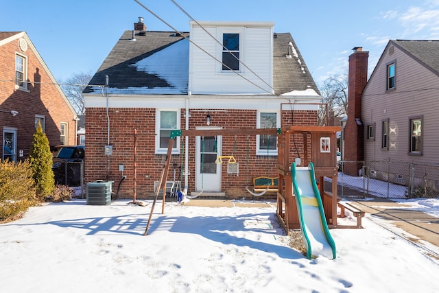 snow covered back of property featuring cooling unit and a playground