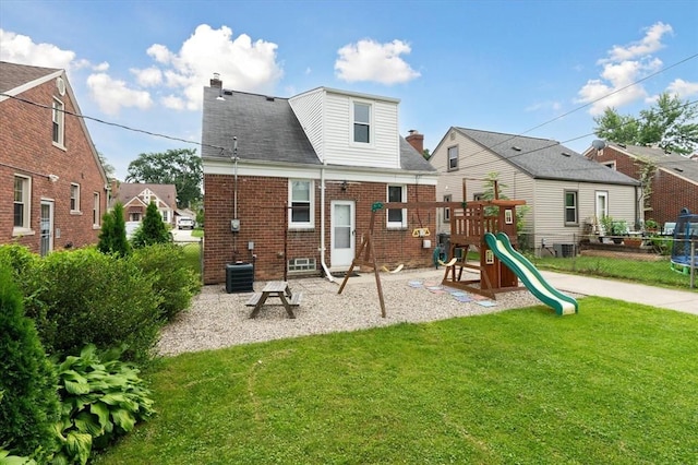 rear view of property featuring a playground and a lawn