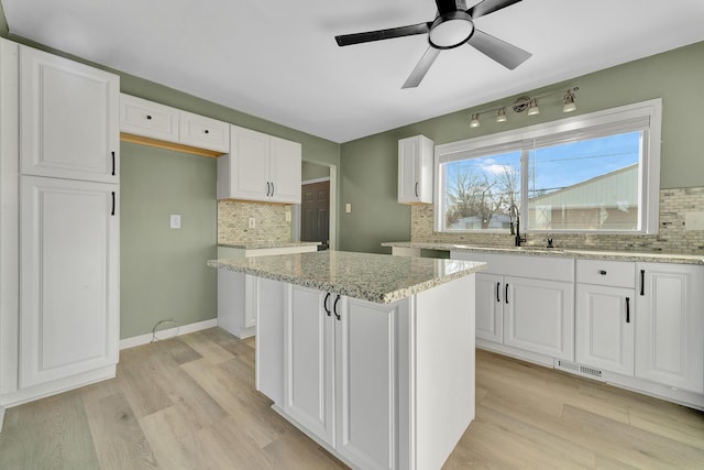 kitchen featuring decorative backsplash, white cabinetry, a kitchen island, and light stone countertops