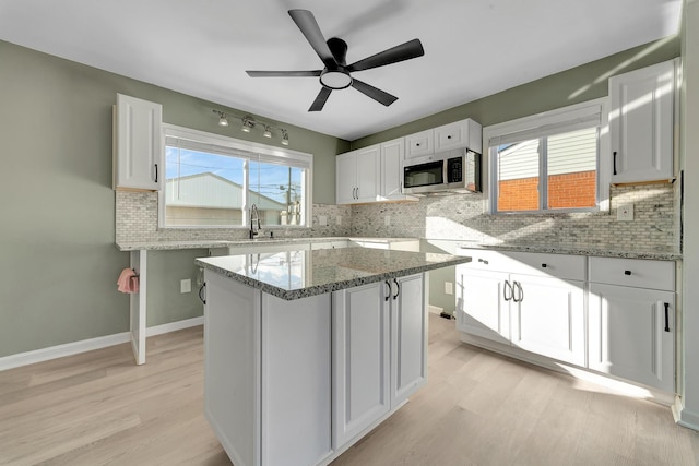 kitchen featuring light stone counters, a center island, white cabinets, and light wood-type flooring