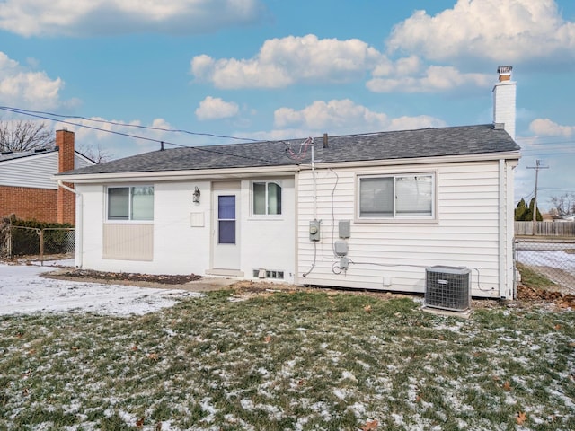 snow covered back of property with a lawn and cooling unit