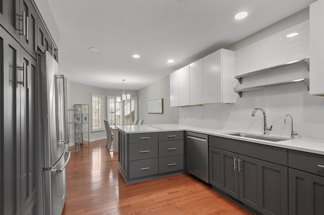 kitchen featuring kitchen peninsula, sink, appliances with stainless steel finishes, decorative light fixtures, and white cabinetry