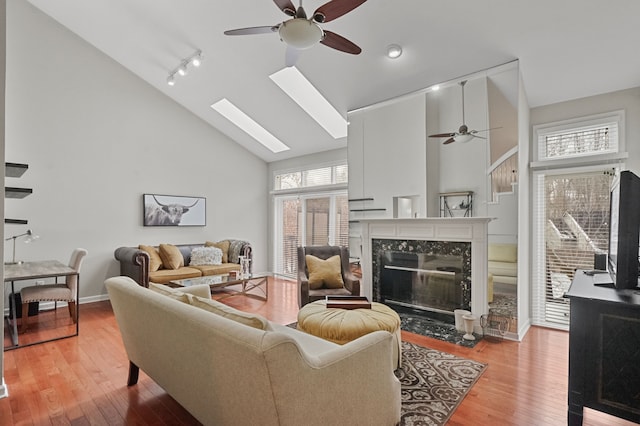 living room featuring a skylight, ceiling fan, light hardwood / wood-style floors, and a premium fireplace