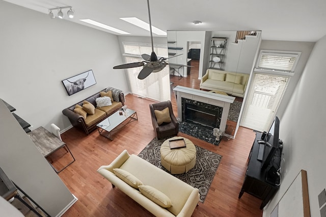 living room featuring a skylight, track lighting, ceiling fan, hardwood / wood-style flooring, and a fireplace