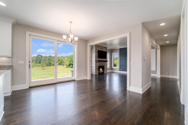 unfurnished living room with dark hardwood / wood-style flooring, a stone fireplace, and a notable chandelier