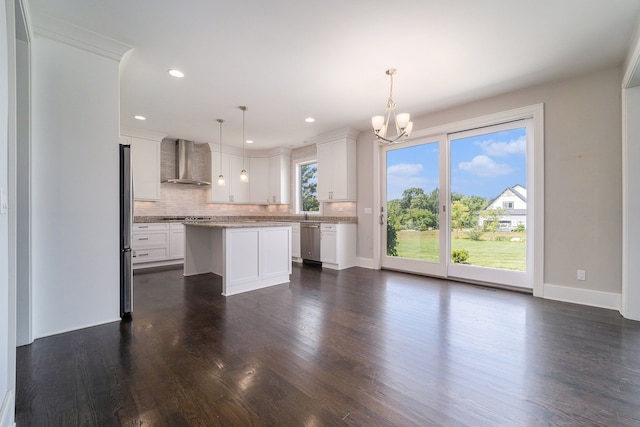 kitchen with wall chimney exhaust hood, stainless steel appliances, hanging light fixtures, a kitchen island, and white cabinets