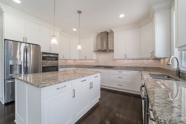 kitchen featuring wall chimney range hood, sink, appliances with stainless steel finishes, decorative light fixtures, and white cabinetry