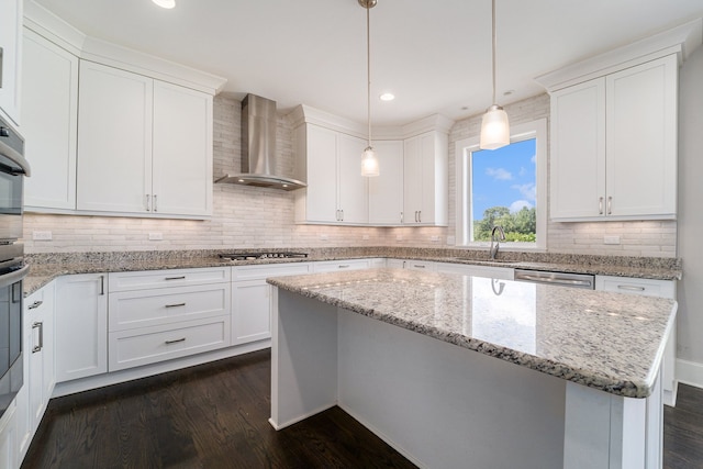 kitchen featuring dark hardwood / wood-style flooring, wall chimney range hood, a center island, white cabinetry, and hanging light fixtures