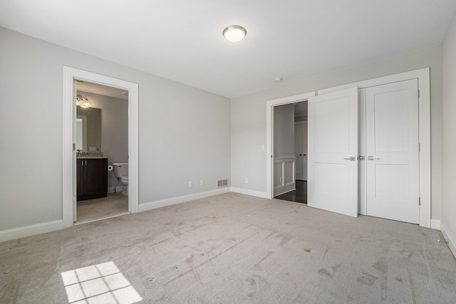 unfurnished bedroom with light colored carpet, ensuite bath, and a closet